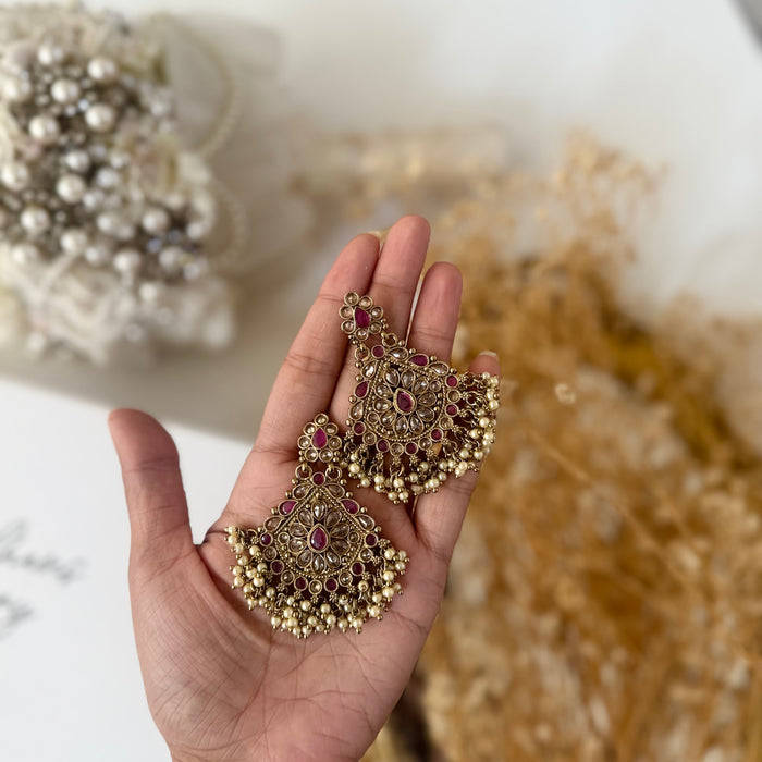 A pair of ornate gold-toned chandelier earrings with fuchsia gemstone accents