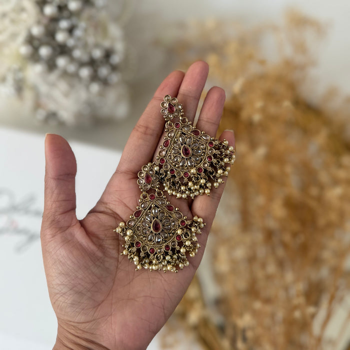 A pair of ornate gold-toned traditional earrings with red and dark brown stones