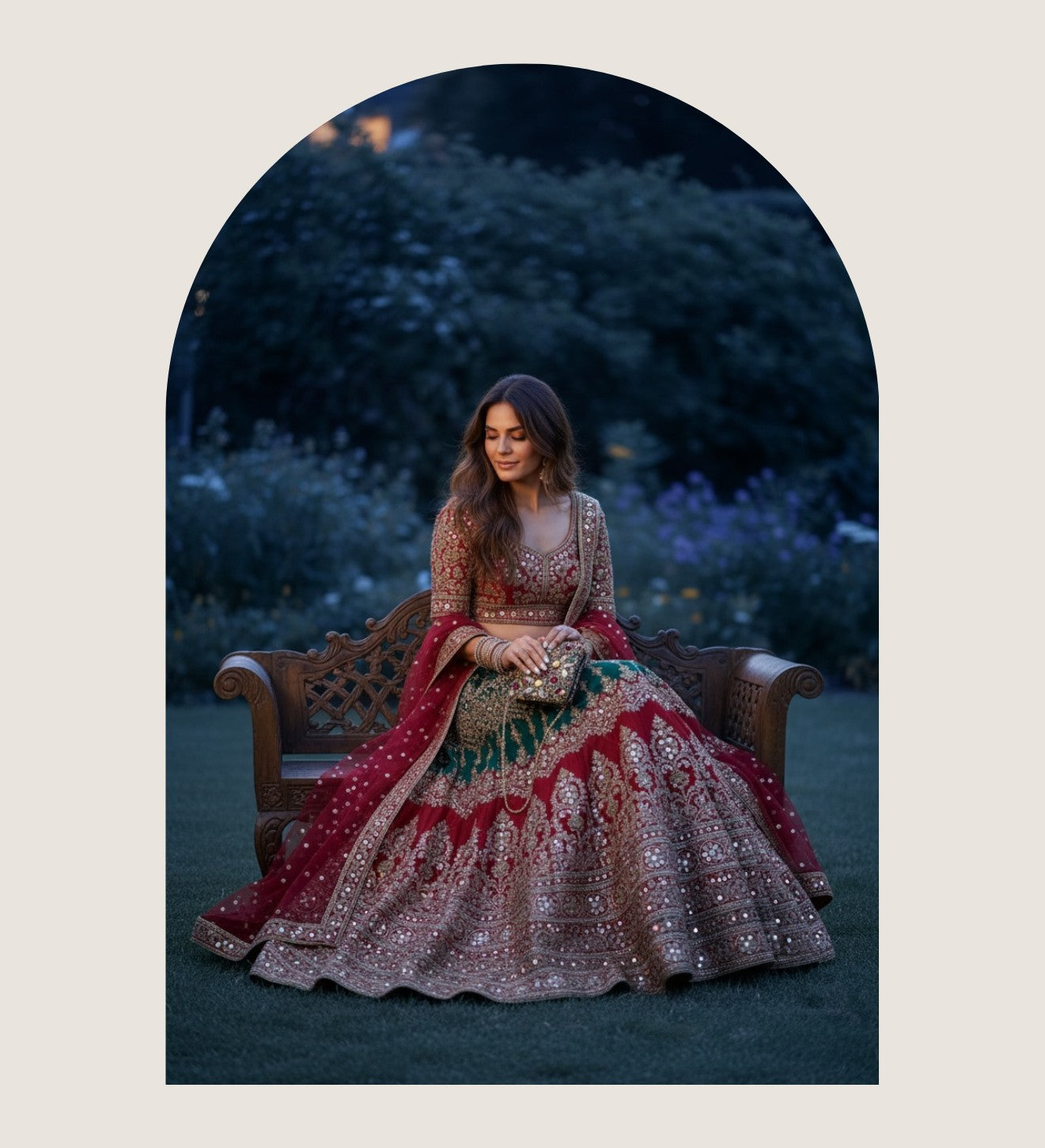 Bride in a red and gold embroidered lehenga seated on a carved bench, holding a jewelled clutch